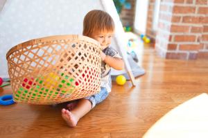 Sensory basket Adorable toddler sitting on the floor playing with wicker basket and balls around lots of toys at kindergarten
