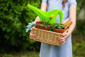 smiling cute girl gardener holding basket and horticultural tools in garden on sunny day. Summer activities