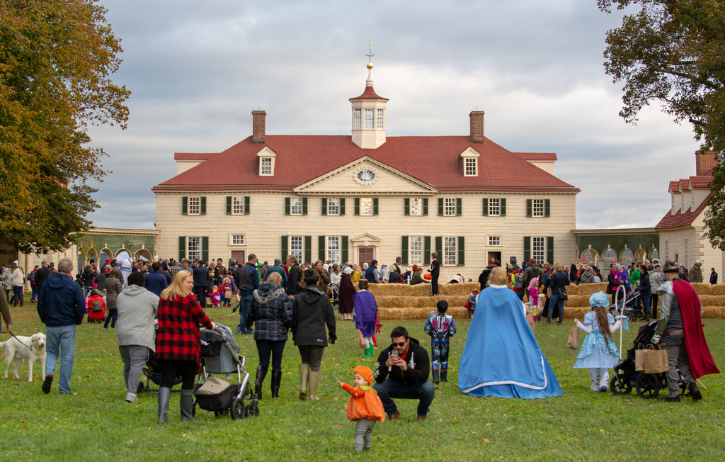 Children dressed as superheroes and witches watch costumed interpreters at a spinning wheel during trick or treating at Mount Vernon
