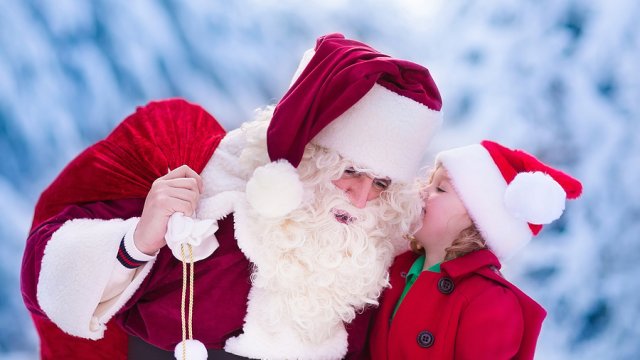 Santa Claus and children opening presents in snowy forest. Kids and father in Santa costume and beard open Christmas gifts. Little girl helping with present sack. Xmas snow and winter fun for family.