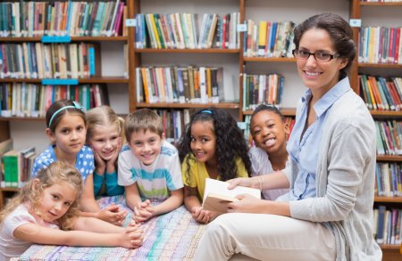 Cute pupils and teacher reading in library at the elementary school