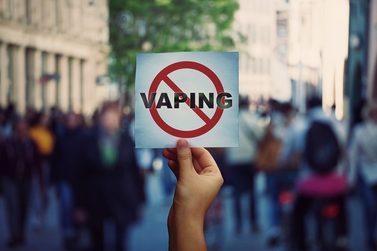 Human hand holding a protest banner stop e-cigarette vaping message over a crowded street background.