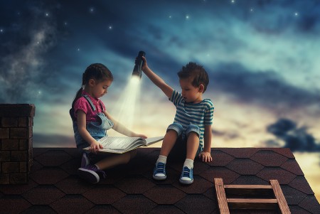 Two children read one of the best night sky books for kids by flashlight on a rooftop under the stars
