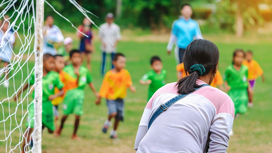 A parent watches from a distance as a child works through a task on their own, building resilience