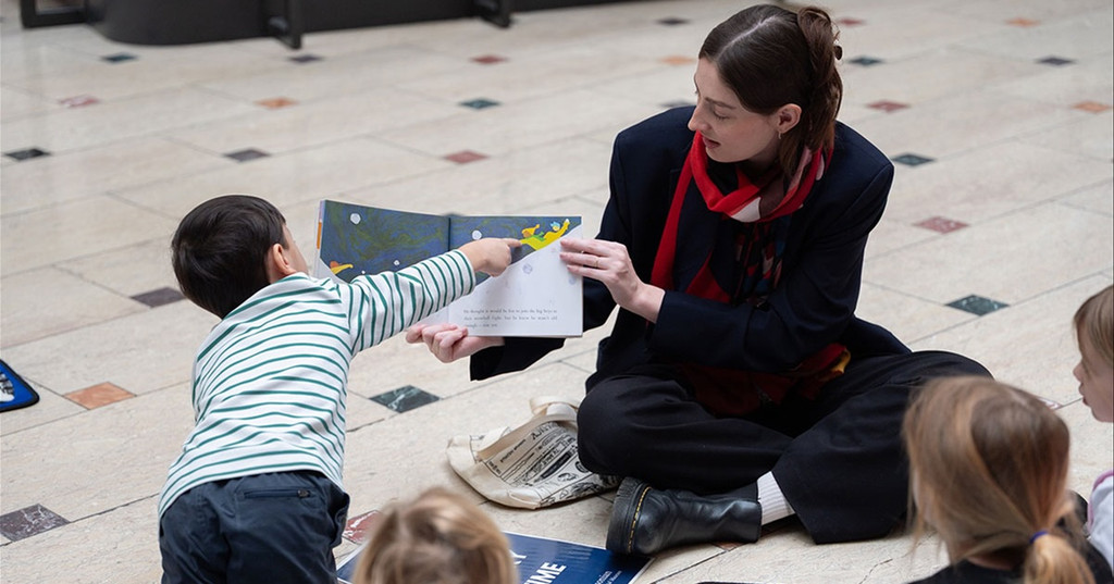 A storyteller reads a picture book to young children seated on the marble floor at Story Time at the National Postal Museum in Washington, DC.