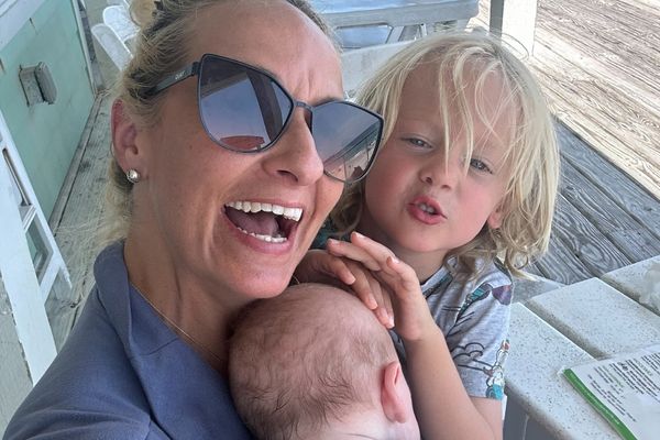 Lauryn Ricketts smiles while holding her baby beside her young son on a porch.