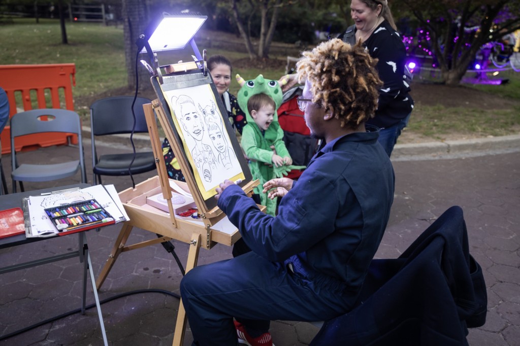 A caricature artist sketches a child in a green dinosaur costume at the National Zoo's Boo at the Zoo