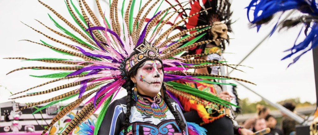 What is Día de los Muertos and where can I celebrate? A dancer in a feathered headdress and sugar skull face paint performs at a Día de los Muertos festival