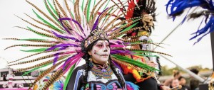 A dancer in a feathered headdress and sugar skull face paint performs at a Día de los Muertos festival