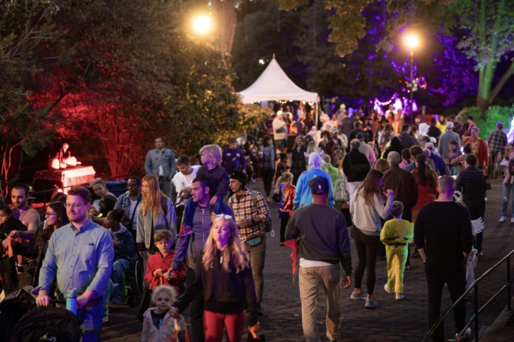 Families in Halloween costumes stroll a zoo path lit in red and purple during Boo at the Zoo.