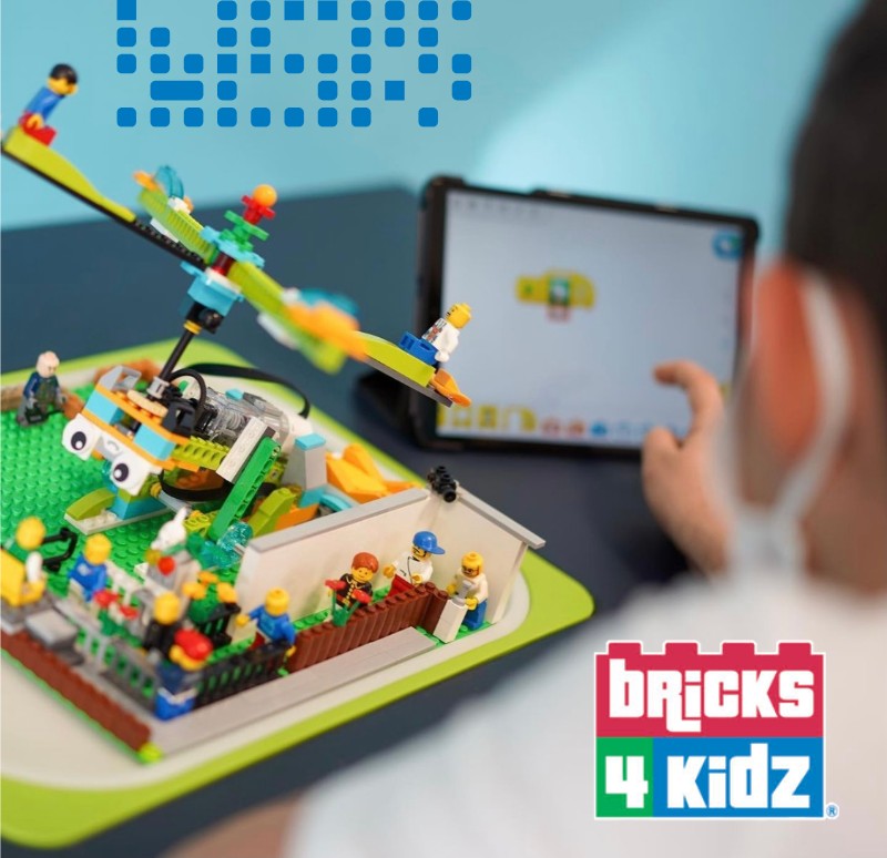 A child uses a tablet to program a motorized LEGO seesaw model with minifigures at a Bricks 4 Kidz class.