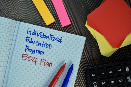 Notebook with Individualized Education Program and 504 Plan handwritten in blue and red marker beside colorful sticky notes